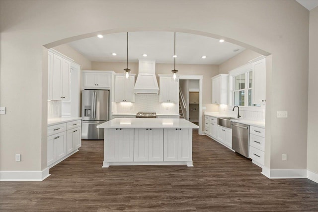 kitchen featuring white cabinets, custom exhaust hood, hanging light fixtures, and appliances with stainless steel finishes