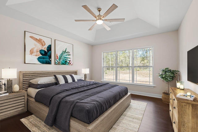 bedroom with a raised ceiling, dark hardwood / wood-style floors, and ceiling fan