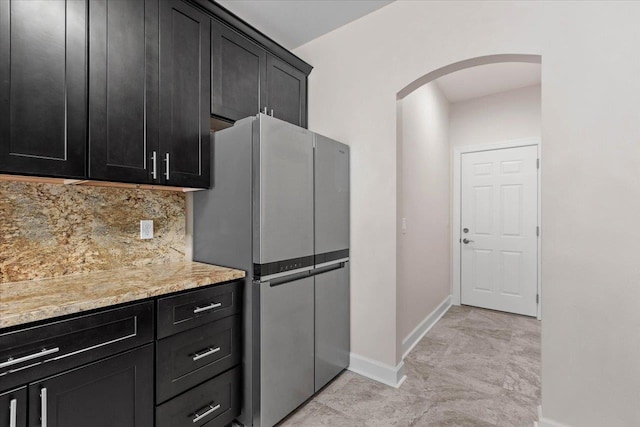 kitchen with light stone counters, backsplash, and stainless steel refrigerator