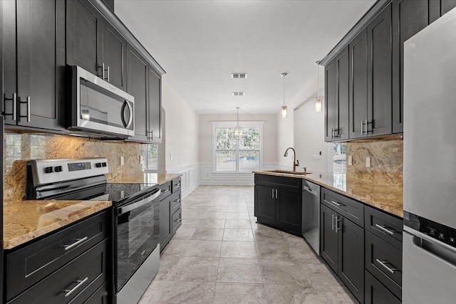 kitchen featuring sink, backsplash, hanging light fixtures, light stone counters, and stainless steel appliances