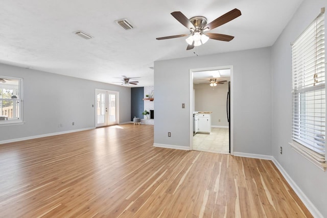 unfurnished living room with a brick fireplace, a wealth of natural light, french doors, and light hardwood / wood-style flooring