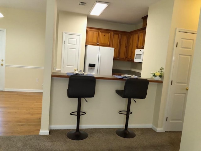 325 Chastain Ln, Tallahassee, FL 32305 - kitchen featuring white appliances, baseboards, a kitchen bar, carpet floors, and brown cabinetry