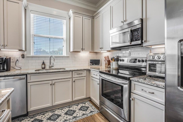 kitchen with sink, light stone countertops, stainless steel appliances, ornamental molding, and white cabinets