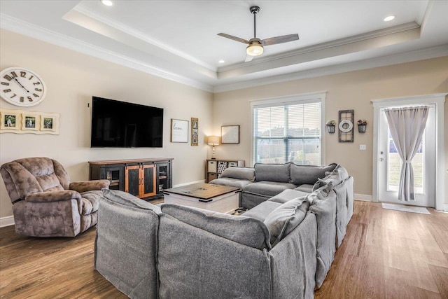 living room with light wood-type flooring, ceiling fan, crown molding, and a raised ceiling