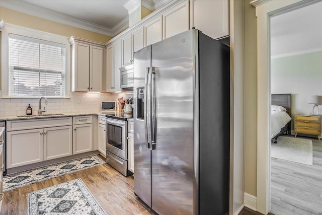 kitchen with light hardwood / wood-style floors, appliances with stainless steel finishes, crown molding, light stone counters, and sink