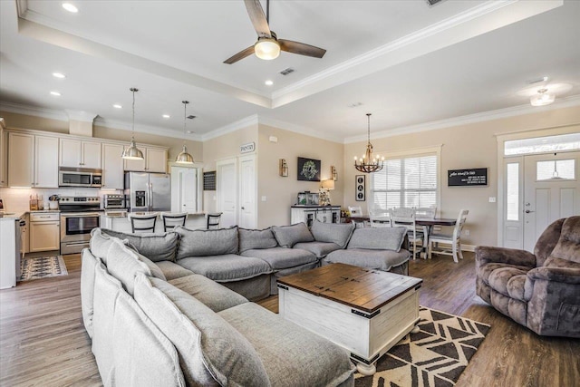 living room featuring dark hardwood / wood-style flooring, crown molding, ceiling fan with notable chandelier, and a raised ceiling