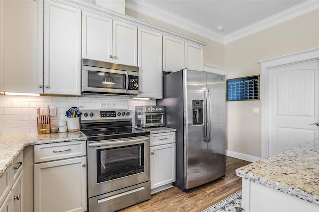 kitchen with light stone countertops, white cabinets, appliances with stainless steel finishes, and ornamental molding