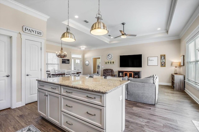 kitchen featuring ceiling fan with notable chandelier, a center island, hanging light fixtures, dark hardwood / wood-style floors, and a tray ceiling