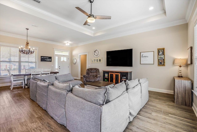 living room featuring a raised ceiling, ceiling fan with notable chandelier, ornamental molding, and hardwood / wood-style floors