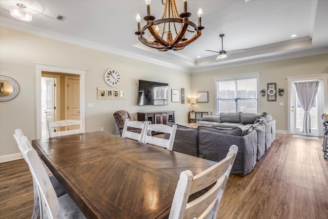 dining area featuring dark hardwood / wood-style flooring, ceiling fan with notable chandelier, and a tray ceiling