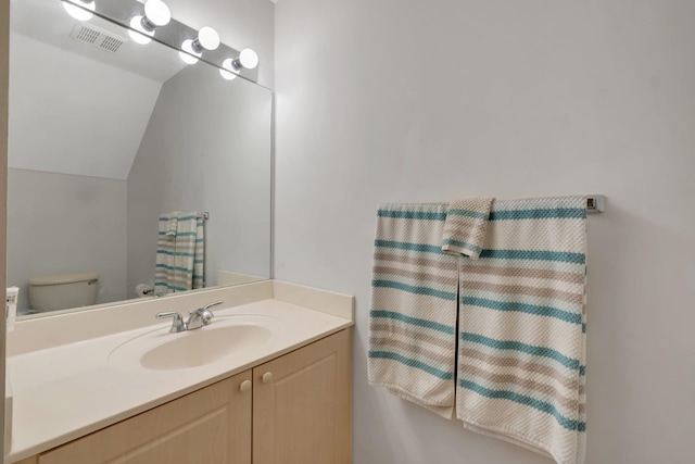 bathroom with toilet, visible vents, vaulted ceiling, and vanity