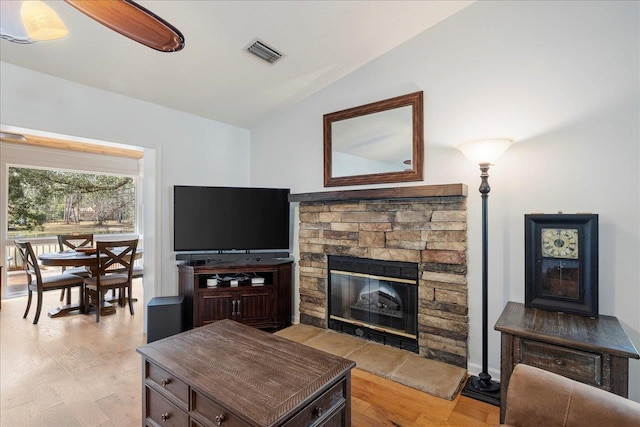 living area featuring light wood-type flooring, lofted ceiling, visible vents, and a stone fireplace