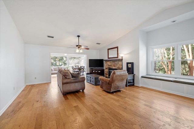 living area featuring light wood finished floors, a stone fireplace, vaulted ceiling, and plenty of natural light