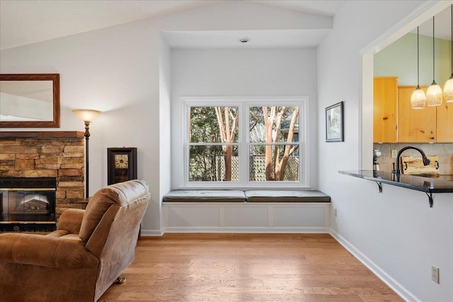 living area with lofted ceiling, light wood-style floors, baseboards, and a stone fireplace