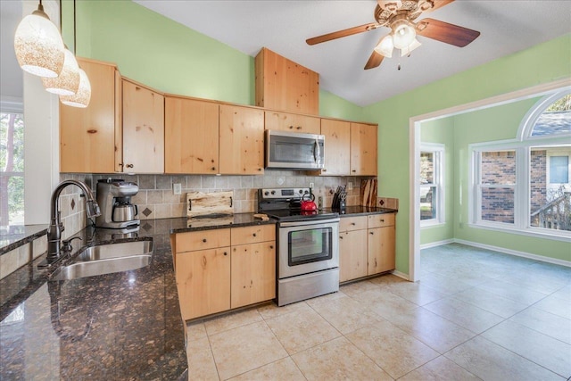 kitchen with stainless steel appliances, hanging light fixtures, light brown cabinetry, a sink, and dark stone counters