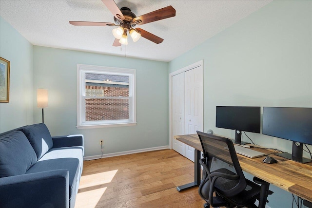 office area featuring light wood-style floors, a ceiling fan, baseboards, and a textured ceiling