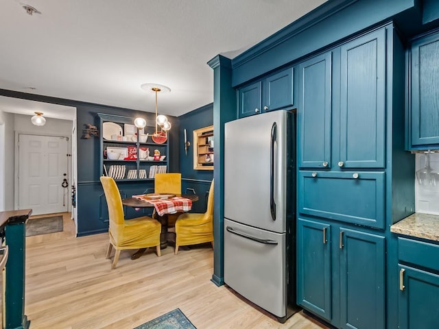 kitchen with blue cabinetry, stainless steel refrigerator, pendant lighting, and light wood-type flooring