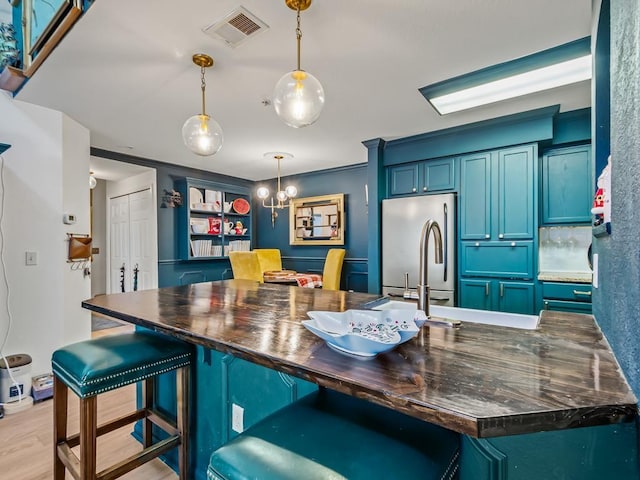 kitchen featuring pendant lighting, stainless steel fridge, blue cabinetry, light hardwood / wood-style floors, and a kitchen bar