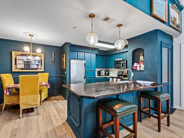 kitchen with pendant lighting, blue cabinets, light hardwood / wood-style flooring, a kitchen bar, and stainless steel appliances