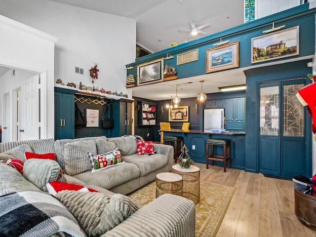 living room featuring light hardwood / wood-style flooring, high vaulted ceiling, ceiling fan with notable chandelier, and ornamental molding