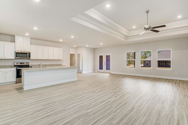 unfurnished living room featuring light wood-type flooring, ceiling fan, ornamental molding, a tray ceiling, and sink