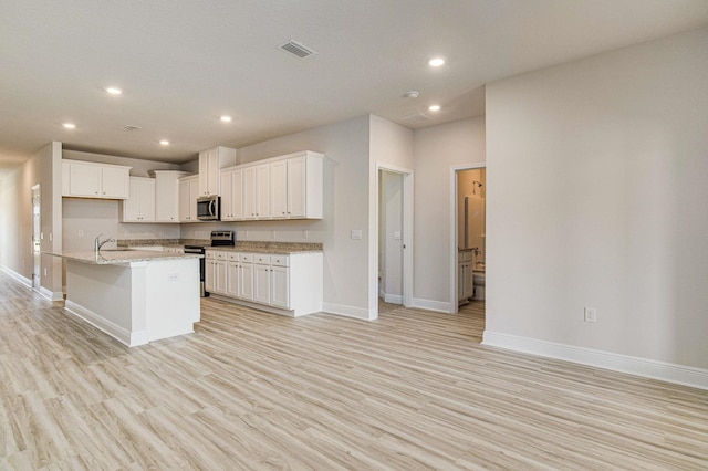 kitchen with light stone counters, a center island with sink, appliances with stainless steel finishes, and white cabinetry