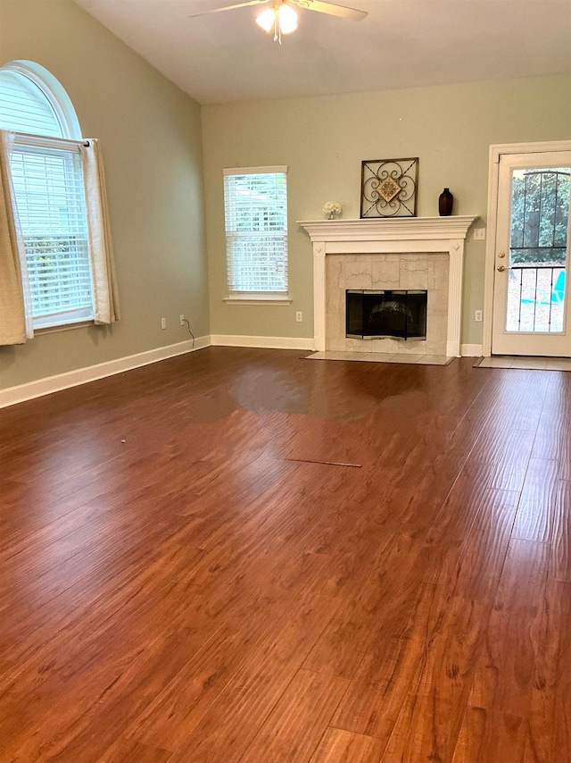 unfurnished living room featuring dark wood-style floors, ceiling fan, a tiled fireplace, and baseboards