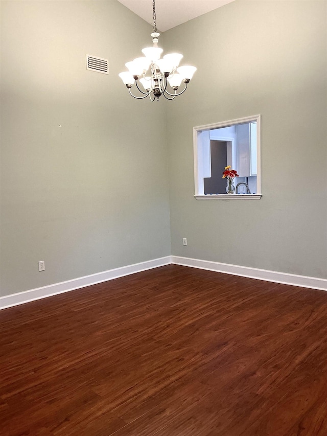 spare room featuring a notable chandelier, visible vents, baseboards, vaulted ceiling, and dark wood-style floors