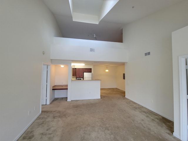 unfurnished living room with ceiling fan, light colored carpet, and a towering ceiling