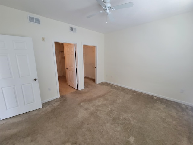 unfurnished bedroom with a spacious closet, a closet, ceiling fan, and light colored carpet