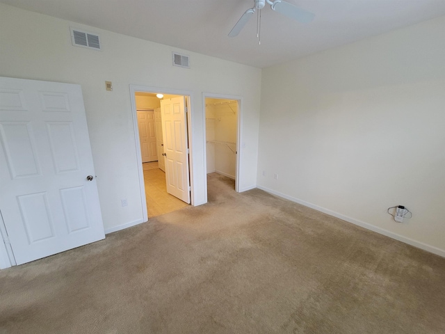 unfurnished bedroom with a walk in closet, a closet, ceiling fan, and light colored carpet