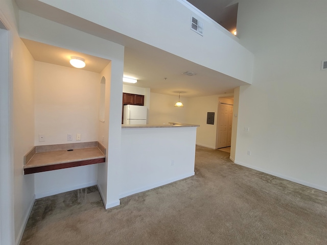 kitchen with kitchen peninsula, light colored carpet, decorative light fixtures, white fridge, and electric panel