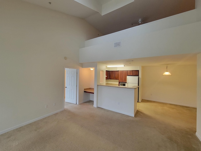 kitchen with kitchen peninsula, light carpet, high vaulted ceiling, white fridge, and hanging light fixtures