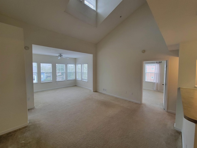 unfurnished living room featuring a skylight, light carpet, high vaulted ceiling, and ceiling fan