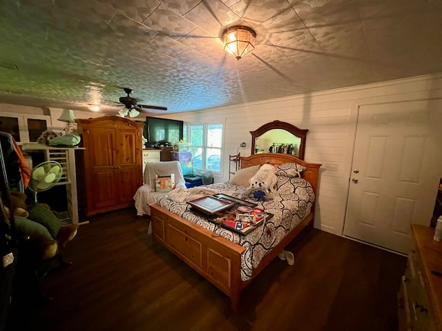 bedroom with dark wood-type flooring, wooden walls, a textured ceiling, and ceiling fan