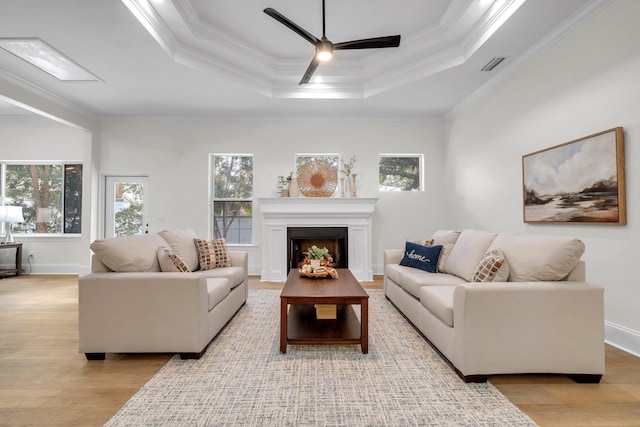 living room with crown molding, a tray ceiling, light hardwood / wood-style floors, and ceiling fan