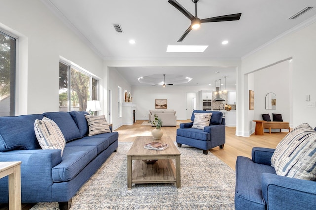 living room featuring ornamental molding, wood-type flooring, ceiling fan, and a skylight