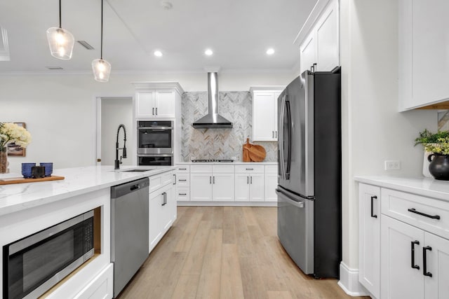 kitchen featuring decorative light fixtures, white cabinetry, sink, stainless steel appliances, and wall chimney exhaust hood