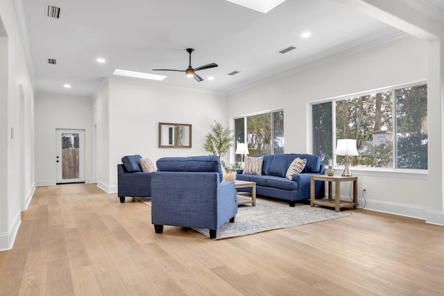 living room with ceiling fan, ornamental molding, a skylight, and light hardwood / wood-style floors