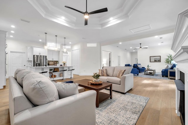 living room featuring crown molding, a tray ceiling, ceiling fan, and light wood-type flooring