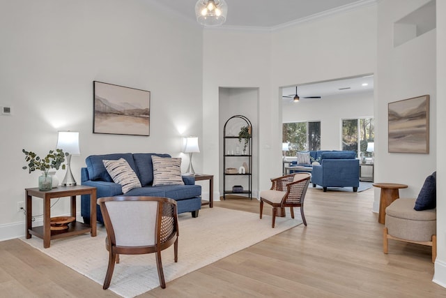 living room with crown molding, a towering ceiling, an inviting chandelier, and light hardwood / wood-style floors