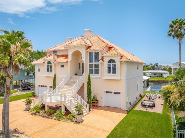 mediterranean / spanish house with a patio area, a water view, a front lawn, and a garage