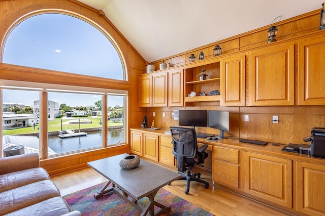 office featuring wooden walls, high vaulted ceiling, built in desk, and light wood-type flooring