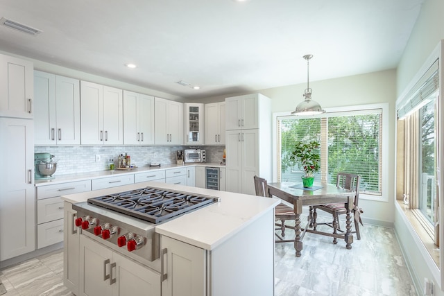 kitchen with tasteful backsplash, beverage cooler, decorative light fixtures, white cabinetry, and stainless steel gas stovetop