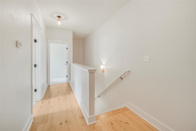 hall featuring baseboards, light wood-style flooring, and an upstairs landing