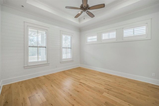 empty room featuring a ceiling fan, baseboards, light wood-style floors, ornamental molding, and a tray ceiling