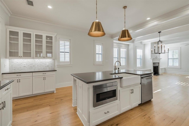 kitchen with light wood finished floors, tasteful backsplash, dark countertops, ornamental molding, and stainless steel dishwasher