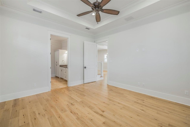 unfurnished bedroom featuring light wood finished floors, a raised ceiling, visible vents, and crown molding