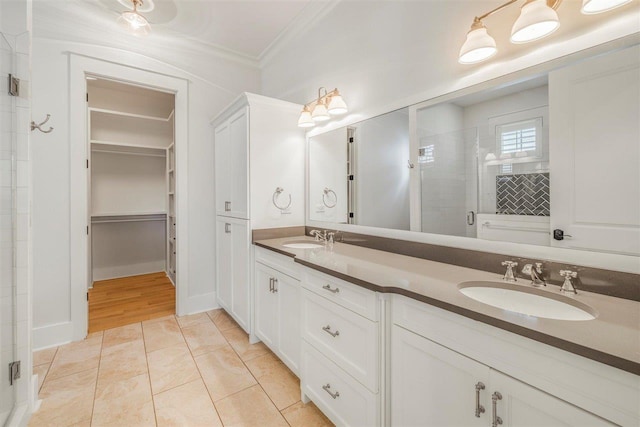 bathroom featuring a stall shower, ornamental molding, a walk in closet, and a sink