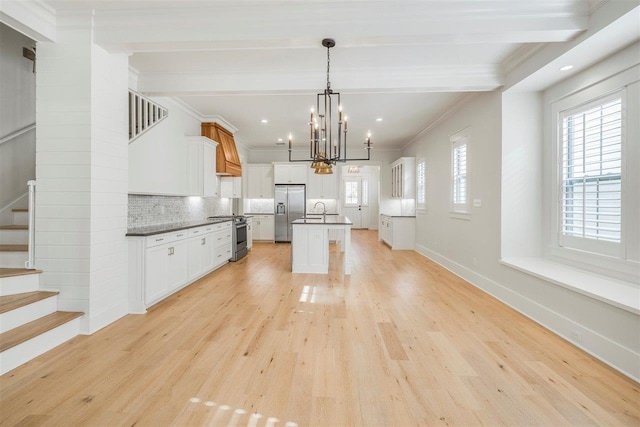 kitchen with tasteful backsplash, an island with sink, light wood-style flooring, stainless steel appliances, and premium range hood